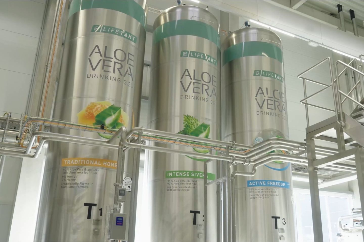 Stainless steel tanks labelled Aloe Vera Drinking Gel in a production hall