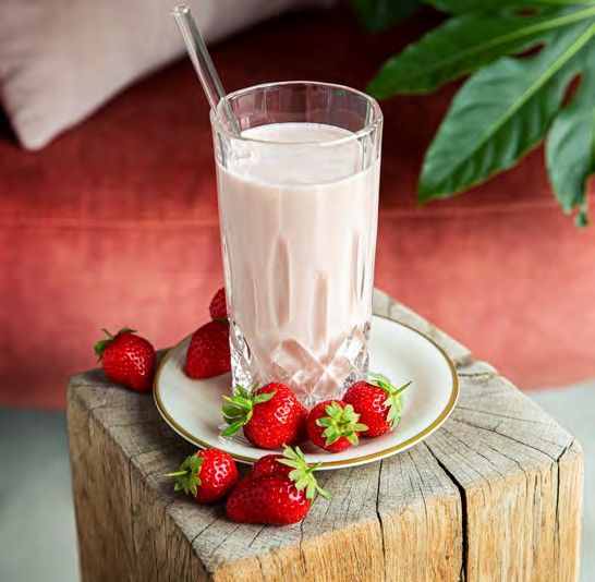 A glass of strawberry shake on a wooden block, with fresh strawberries beside it